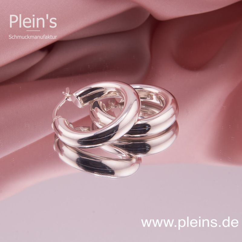 Preview: Detailaufnahme der hochglanzpolierten Silber Creolen, liegend auf einer glatten Oberfläche.